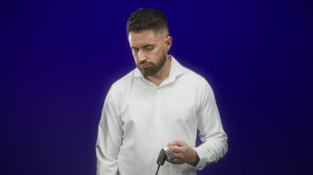 Hispanic man with beard holding car keys in hand and looking down in studio; pensive quiet reflection.