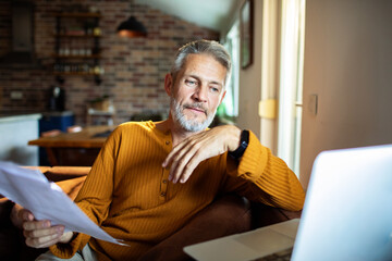 Obraz premium Mature man reviewing finances on laptop at home