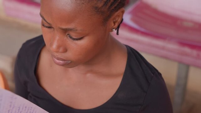 Focused female learner reading notes diligently. Casual young woman concentrates deeply on her study session. Relaxed female student engaged in attentive review of study materials outdoors
