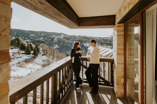 Couple enjoys warm drinks on balcony with mountain view in winter afternoon