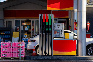Gas station refueling pumps with hoses and price display, parked car beside convenience store doors, safety cone and fire extinguisher on site © K
