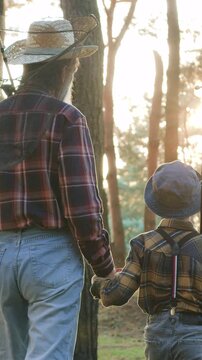 Slow motion of attractive positive friendly grey-bearded senior fishman in straw hat which holding by hand his dutiful small grandchild when going fishing with fishing tackles to the lake,passing