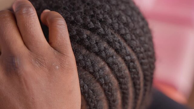 black woman inspecting braided scalp closely, gentle hand revealing dry flakes on textured cornrows, warm pink background, intimate home setting, parental touch checking edges and product residue