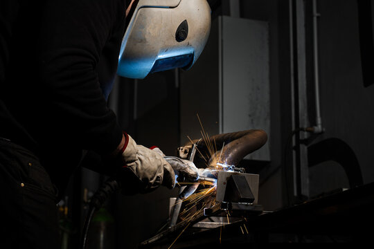 Worker performs shielded arc welding joining steel with sparks