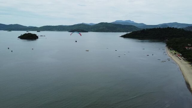Tandem paramotor flying close to the Jabaquara Beach and over the water, with a stunning view of the Paraty bay, the small islands and the mountains covered with dense Atlantic forest in Brazil