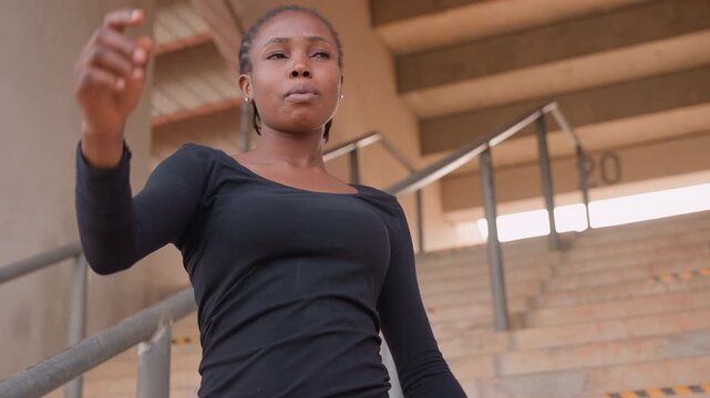 woman on concrete steps gesturing confidently aspiring speaker rehearses a speech, open posture, supportive railing and repeating stairs, natural light, leadership energy and persuasive expression.