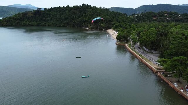 Tandem paramotor flying along Jabaquara Beach, over the water, with a stunning view of the Paraty bay and the mountains covered with dense forest in Paraty, Brazil