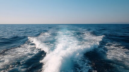A powerful white wake churns the deep blue ocean leaving a trail of foam behind a fast moving boat towards the clear horizon under a bright sky