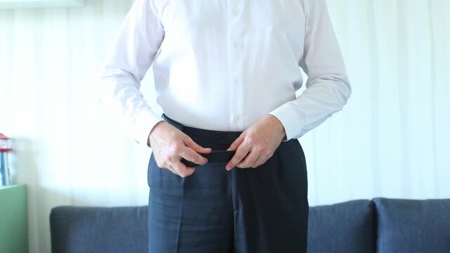 A man fastens a black belt over dark trousers and a white shirt, emphasizing precision, readiness, and the quiet dignity of daily preparation.
