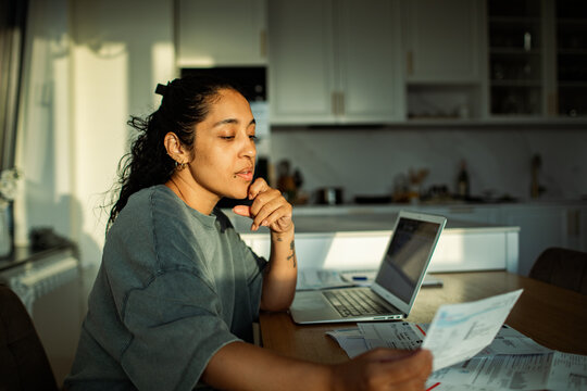 Young woman reviewing bills on laptop at kitchen table