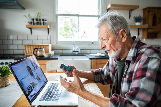 Senior man consulting doctor online with inhaler at home kitchen