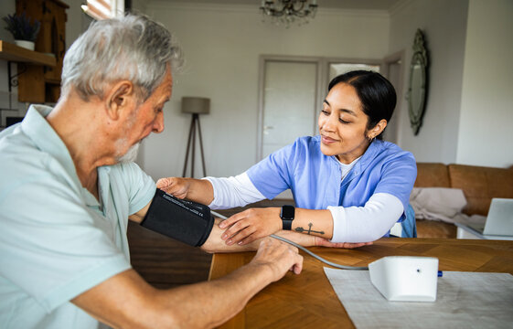 Home nurse checking senior man's blood pressure in living room