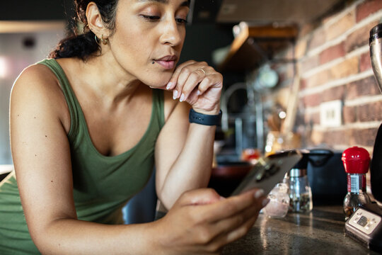Focused woman checking smartphone in home kitchen