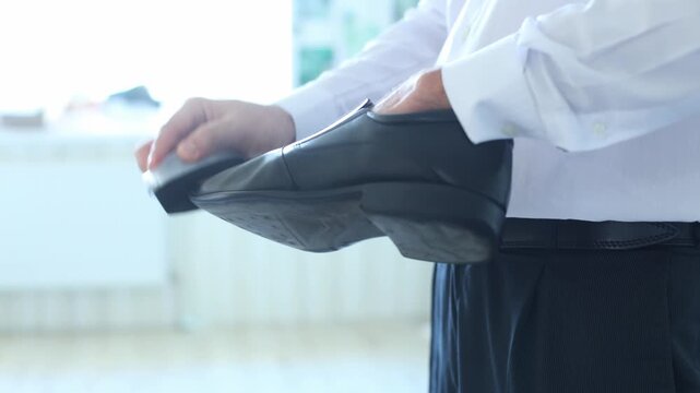 A man in a white shirt and dark trousers meticulously polishes a black dress shoe, evoking care, professionalism, and the quiet dignity of daily preparation.