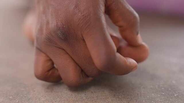 closeup black child toes checking for splinter and grit, tender fingers probing between toes on dusty concrete, warm skin tones, subtle anxiety and gentle care, home environment, pediatric hygiene