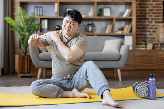 Man experiencing intense shoulder pain and discomfort during an intense workout routine on a yoga mat at home, indicating a potential muscle strain or injury from exercise