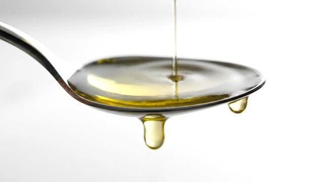 Olive oil pouring into spoon isolated against white background