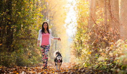Obraz premium The girl is walking along the forest with her husky dog