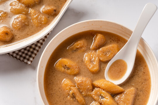 Top view of Kolak pisang on a white plate with a white spoon. Indonesian dish for breaking the fast, during Ramadan or Eid al-Fitr. Sweet soup made from bananas with coconut milk and brown sugar. 
