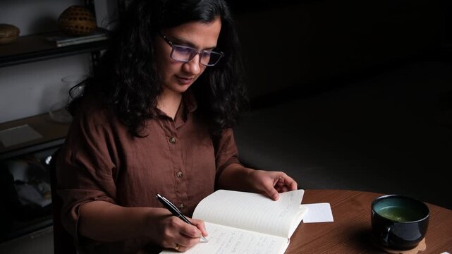 woman writing in notebook at her home office desk late at night, entrepreneur, business woman, deadlines, hustler
