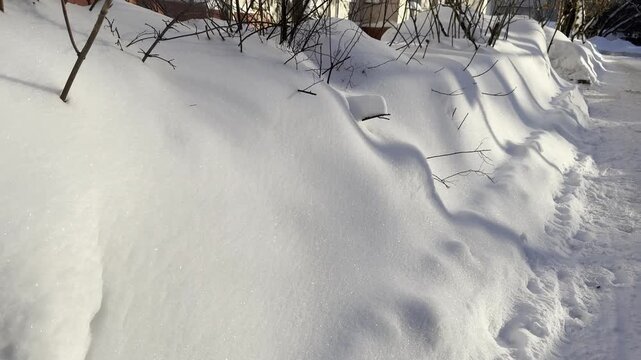 The camera moves along a large snowbank by the roadside, capturing textured layers of packed snow under cold winter light. The motion creates a dynamic perspective as the white surface stretches into 