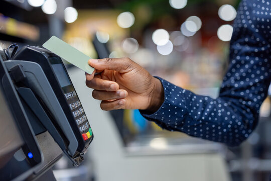 Person's hand holding a credit card near a pos terminal, performing a secure and quick contactless payment transaction in a retail store representing modern shopping and financial technology