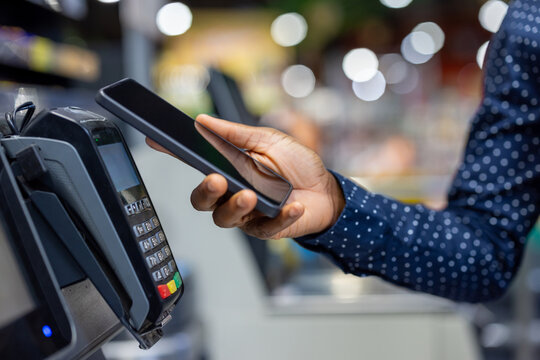 Person using a mobile phone to make a contactless payment at a point of sale terminal in a retail environment, illustrating modern digital transaction convenience
