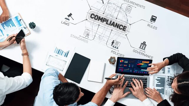 A group of professionals collaborates on compliance strategies, analyzing charts and data on laptops in a modern office setting, focusing on rules and regulations. Raster