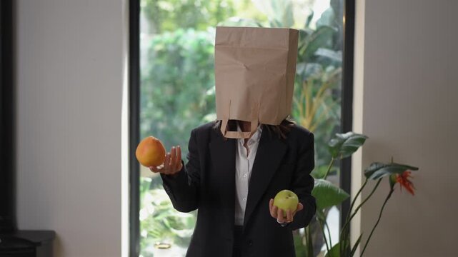 Anonymous businesswoman in a suit with a paper bag over her head juggling an orange and an apple. The concept of multitasking and stress