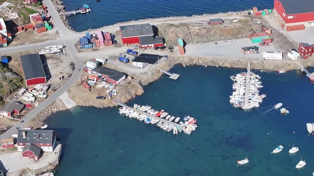 Wide shot of Tasiilaq town and harbor in East Greenland. The footage captures the colorful wooden houses, small boats in the marina, and a dramatic mountain backdrop shrouded in low-hanging clouds 