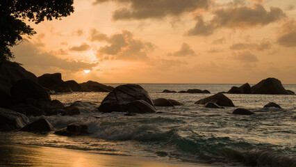 A peaceful sunset over a rocky beach in the Seychelles, with gentle waves, golden light, and a calm tropical atmosphere - perfect for a relaxing vacation escape.
