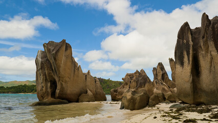 A peaceful tropical beach in the Seychelles with dramatic granite rock formations, clear shallow water, and a bright blue sky, capturing a relaxing island vacation atmosphere.
