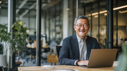 Fototapeta premium Happy mature Asian businessman with glasses working on a laptop in a modern office