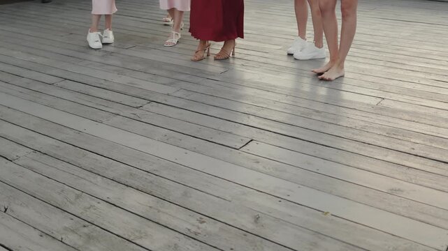 bridesmaids feet with caucasian group standing on wooden deck showing heels, flats and sneakers, prewedding