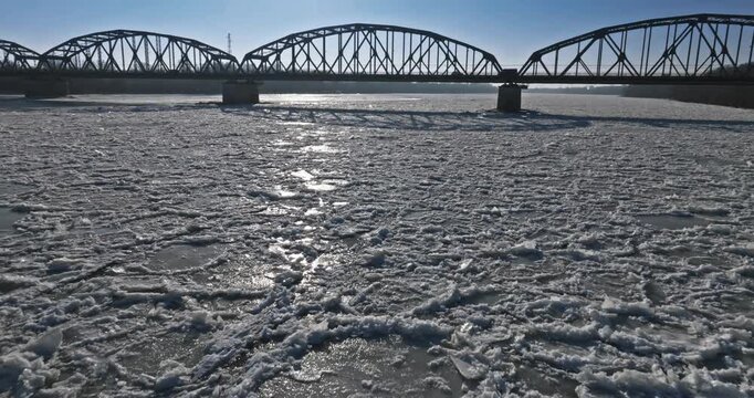 Floe on the frozen Brda River with a metal bridge.
