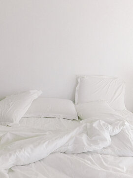 Minimal white resort bed with unmade sheets and clean wall for luxury hospitality and lifestyle branding