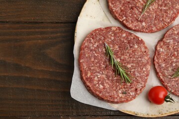 Obraz premium Uncooked meat patty with rosemary and tomato on wooden table, flat lay. Space for text