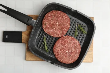 Fotobehang Eten Uncooked meat patty with rosemary in frying pan on white tiled table, top view  © New Africa