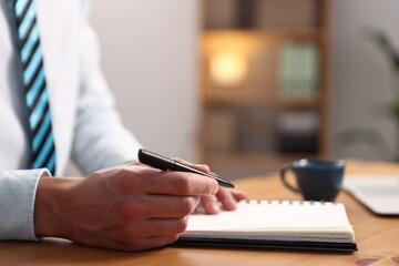 Fototapeta premium Man writing in notebook with pen at wooden desk, closeup