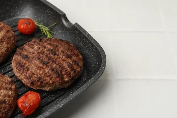 Fotobehang Eten Delicious grilled meat patties, tomatoes and rosemary in grill pan on white tiled table, closeup. Space for text  © New Africa