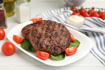 Delicious grilled meat patties, tomatoes and spinach on white tiled table, closeup