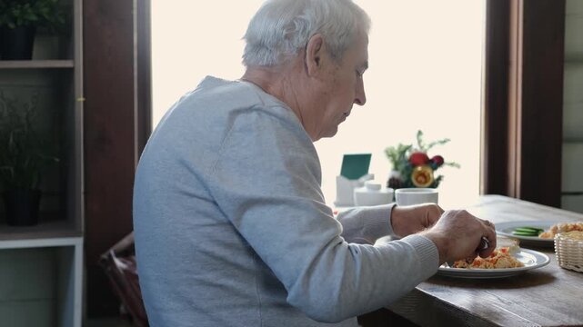 Happy senior man eating a scramble on a white plate with vegetables. Elderly male using knife and fork to cutting meal, has a breakfast. Balanced diet, cooking, culinary. Food concept. Old person