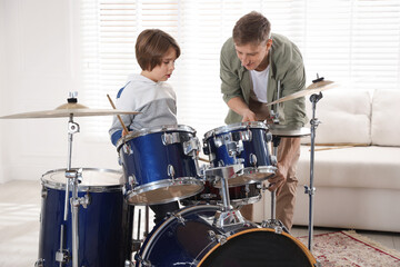 Little boy learning how to play drums with music teacher indoors