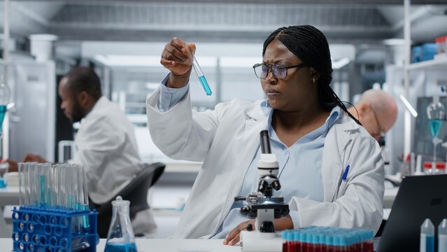 Lab materials scientist investigating blue liquid polymer properties in test tube container. Researcher testing new synthetic material durability and viscosity in lab, camera B
