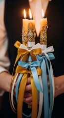 Obraz premium Woman holding three lit decorative candles adorned with golden, white, and blue ribbons. Religious ceremony essential for Palm Sunday.