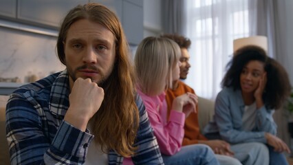 Obraz premium Depressed Caucasian man think at home solving problem anxious male feeling isolated antisocial avoiding friends introvert suffering ignoring social life while multiethnic women men having fun together