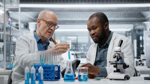 Teamworking lab researchers evaluating blue compound solution for new drug formulation. Team of research facility colleagues testing experimental medication properties in vial, camera A