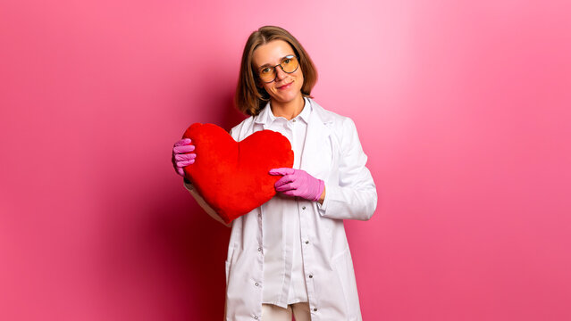 Portrait of a doctor holding a heart in her hands signifies the importance of a health check-up. Smiling cardiologist or gynecologist holds a plush heart