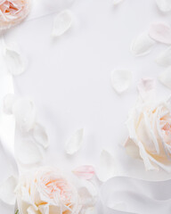 Vertical floral frame with white and blush roses petals on soft light background.