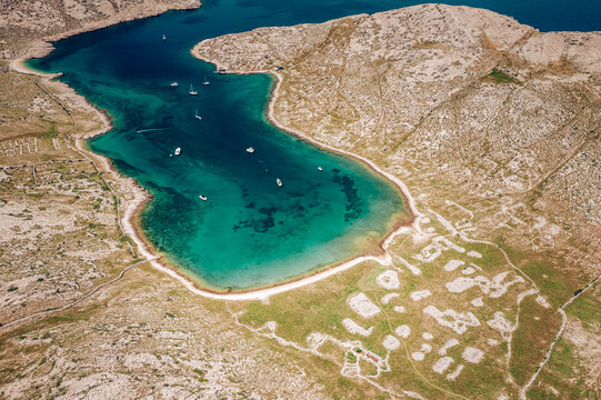 Aerial view of turquoise waters meeting the rugged coastline, dotted with boats and framed by arid hills, Baska, Primorje-Gorski Kotar County, Croatia.